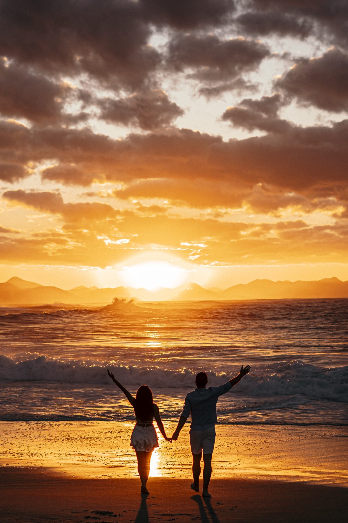 Mayra e Jason de mãos dadas na praia ao pôr do sol